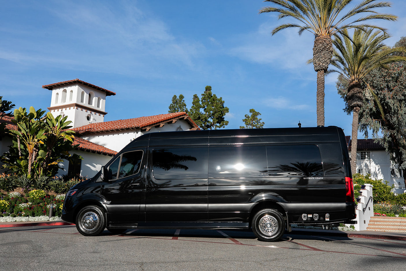 Sleek black Ultimate Coach Sprinter luxury van, an ideal RV rental, parked by a beautiful Spanish-style building.