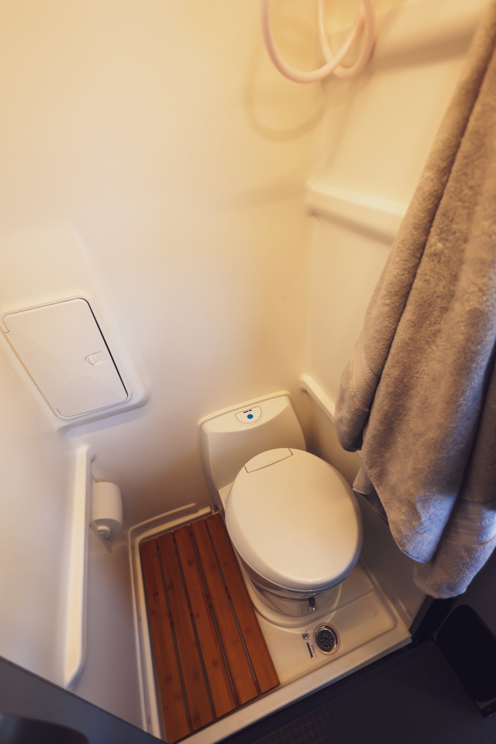 This RV rental's compact wet bath features a white toilet, shower hose, drain, and a practical wooden slatted mat.