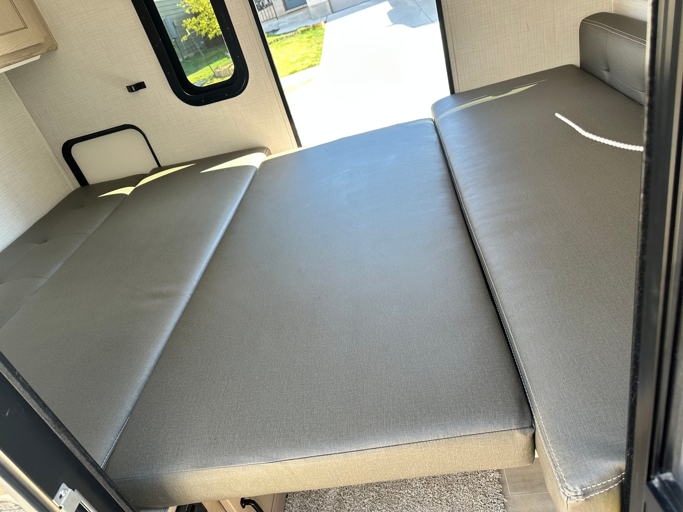 Spacious RV rental interior with a gray convertible bed and bright window view, ready for your camper trip.