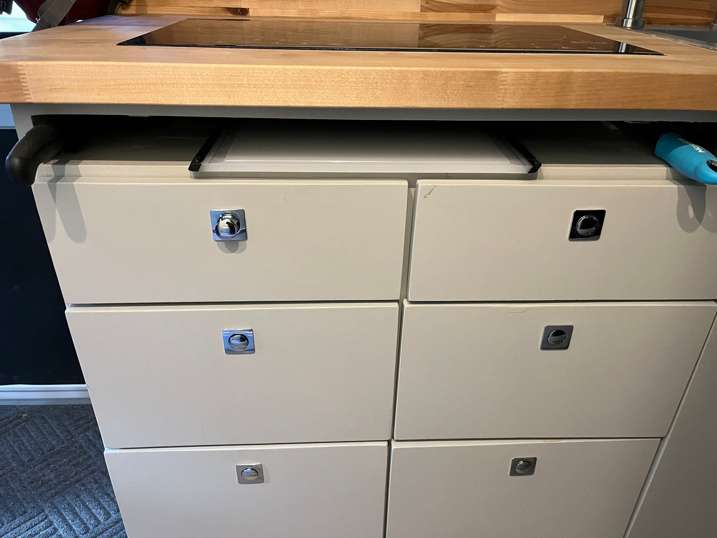 RV rental kitchen space: light wood counter with induction hob, pull-out cutting board, and compact storage drawers.