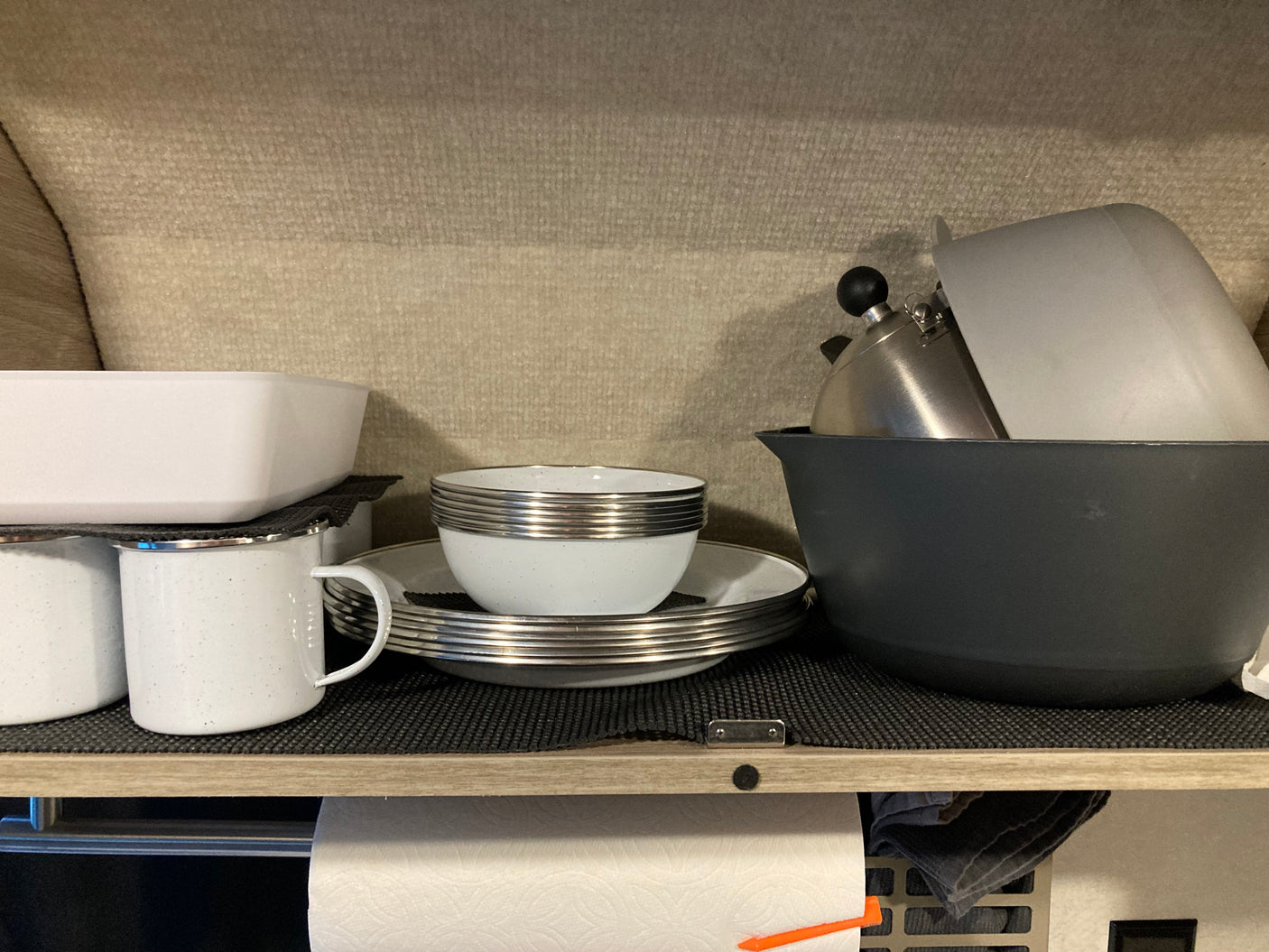 Compact kitchen storage in an RV rental: organized white dishes, mugs, kettle, and paper towels on a shelf.