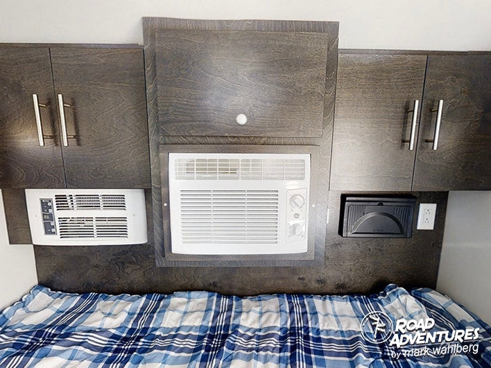 Comfort in your RV rental: a compact sleeping area with two built-in AC units, dark wood cabinets & plaid bed.