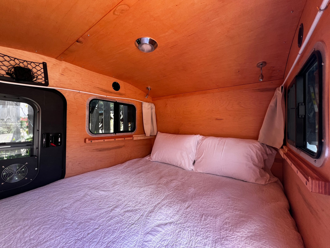 Explore a compact RV rental interior with a comfy bed, wooden accents, and functional windows for cozy mobile sleeping.