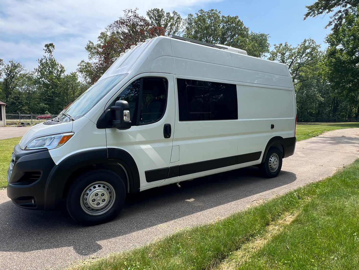 White high-top camper van, a versatile RV rental, parked on an asphalt drive. Features tinted windows & roof setup.