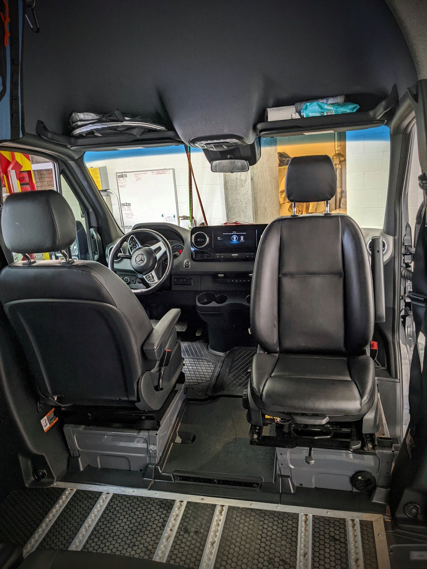 Inside a Mercedes-Benz van, likely an RV rental, with front seats, dashboard, and configurable floor.