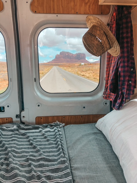 Cozy RV rental with a bed, showing a long desert road through the window leading to a majestic mesa.