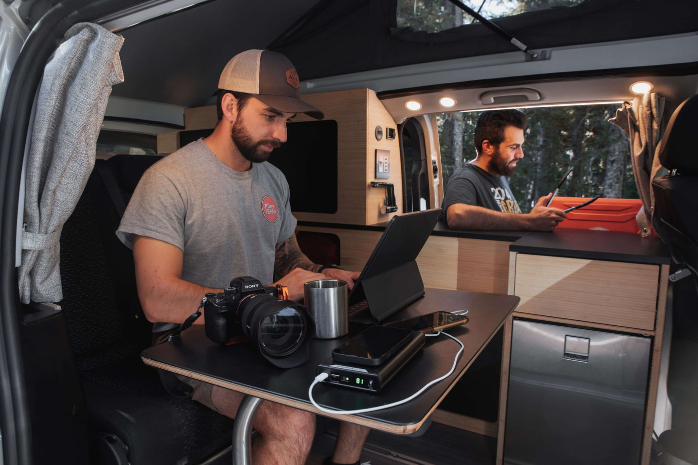 a person cooks in a pop-top camper van's kitchen. Cozy mobile living with a bed.|Dark blue RV rental van on a gravel road — photo 7
