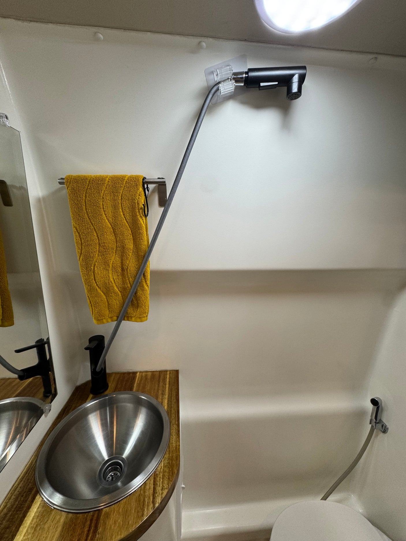 Compact rv rental wet bath featuring a sink, pull-out shower faucet, toilet, and bidet sprayer. Efficient small space design.