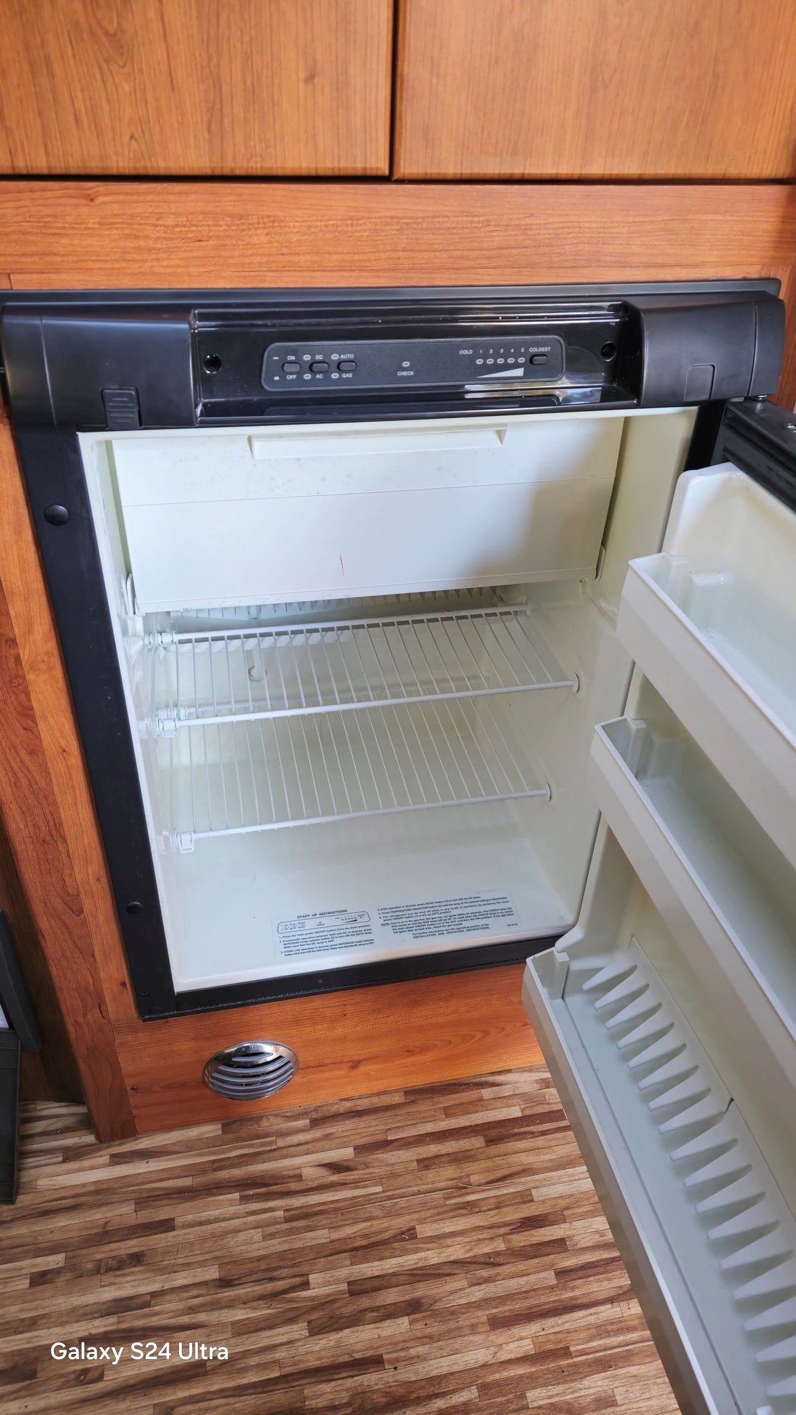 RV rental refrigerator, open and empty. Control panel shows temp settings (cold to coldest) and power options (ON/OFF, DC/AC/Gas).