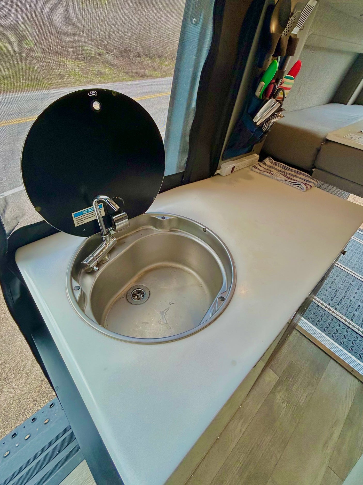 Compact RV rental kitchen features a stainless steel sink with cover and utensil storage, perfect for on-the-go travel.