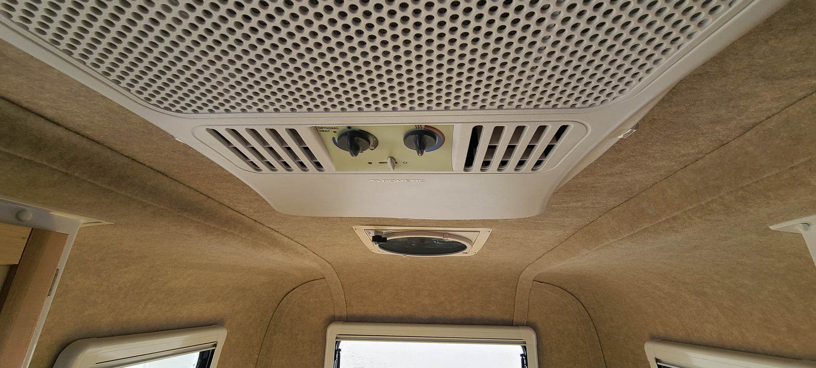 This RV rental's ceiling features a Dometic AC/heater unit, vents, and a light brown fabric lining, with windows below.