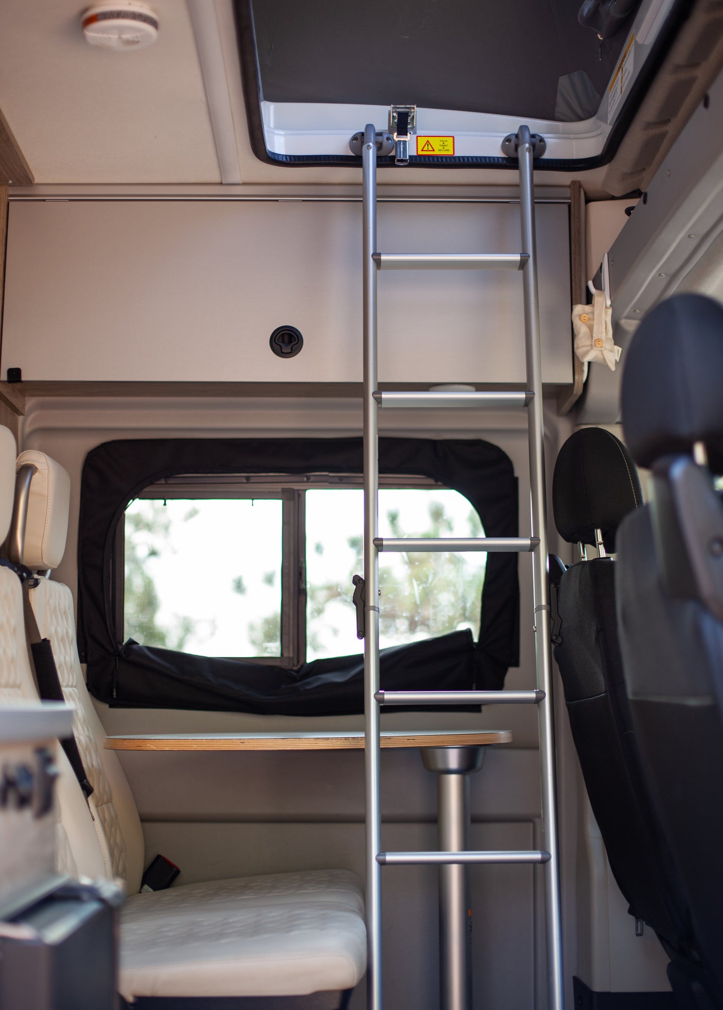 Interior of an RV rental: a ladder to an upper bunk, a table with a sink, and seating, ready for adventure.