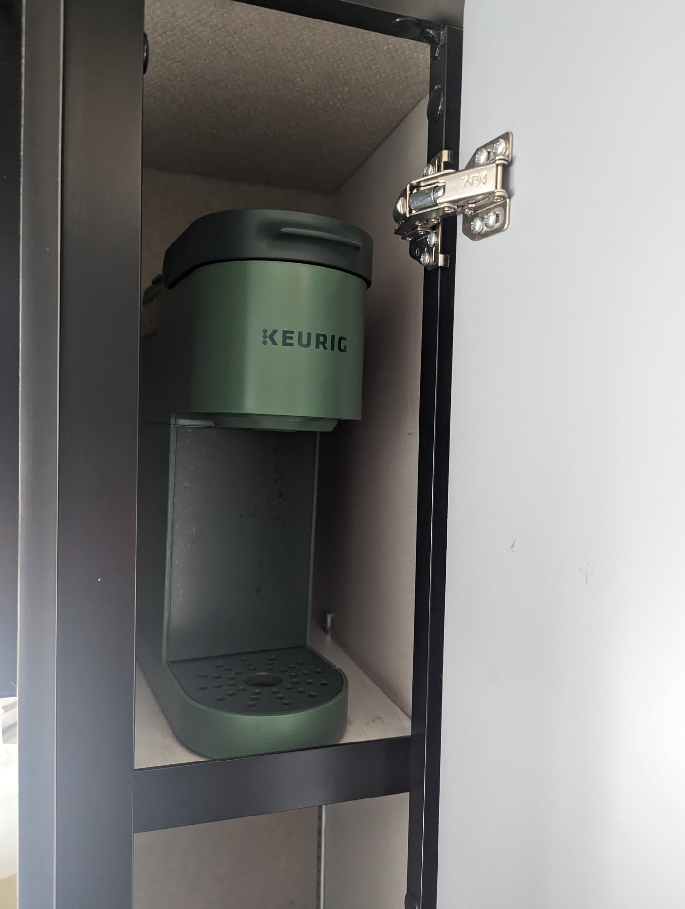 Compact green Keurig coffee maker on a shelf inside an RV rental cabinet, door open for access.