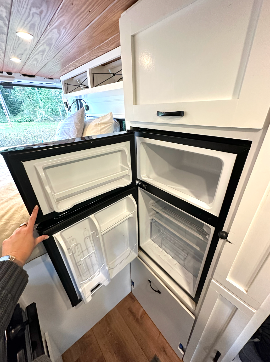 RV rental interior: A compact refrigerator and freezer are open, showcasing efficient food storage in this modern van conversion.