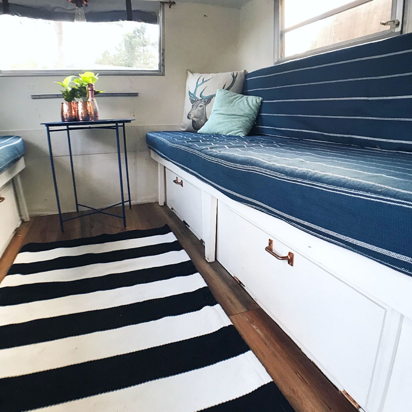 Bright RV rental interior: blue striped cushions, white storage, copper accents, and a striped rug create a cozy space.