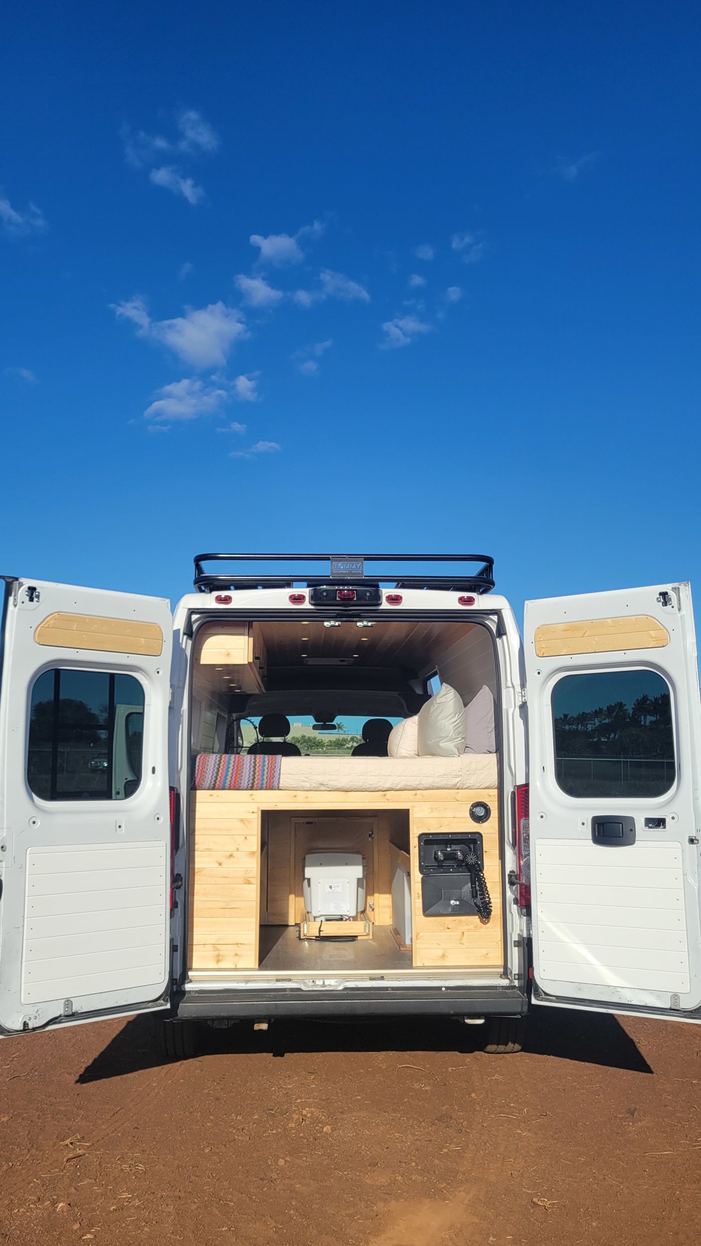 RV rental: Back view of a white camper van revealing its cozy interior with a bed, wood cabinetry, and toilet.