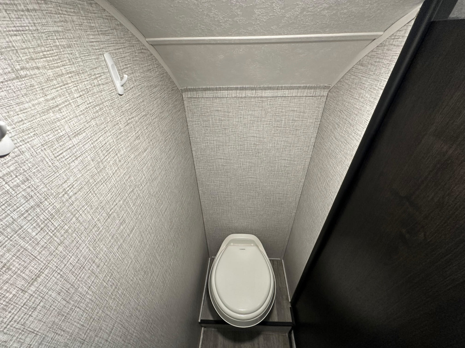 Compact RV rental bathroom interior featuring a white toilet, textured grey walls, and a convenient wall hook.