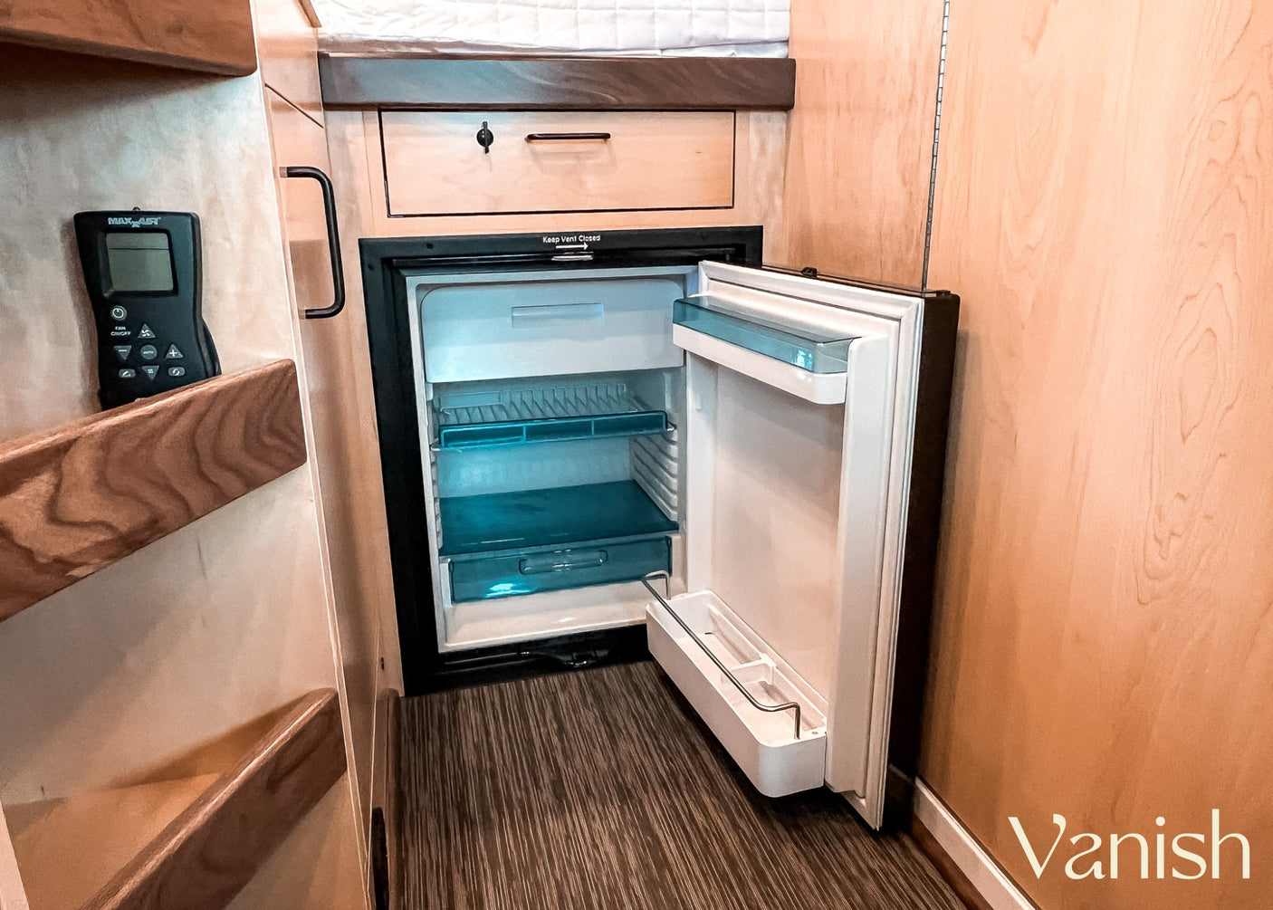 Compact RV rental interior with an open fridge, drawer, and MAX-AIR remote. Efficient mobile living space.