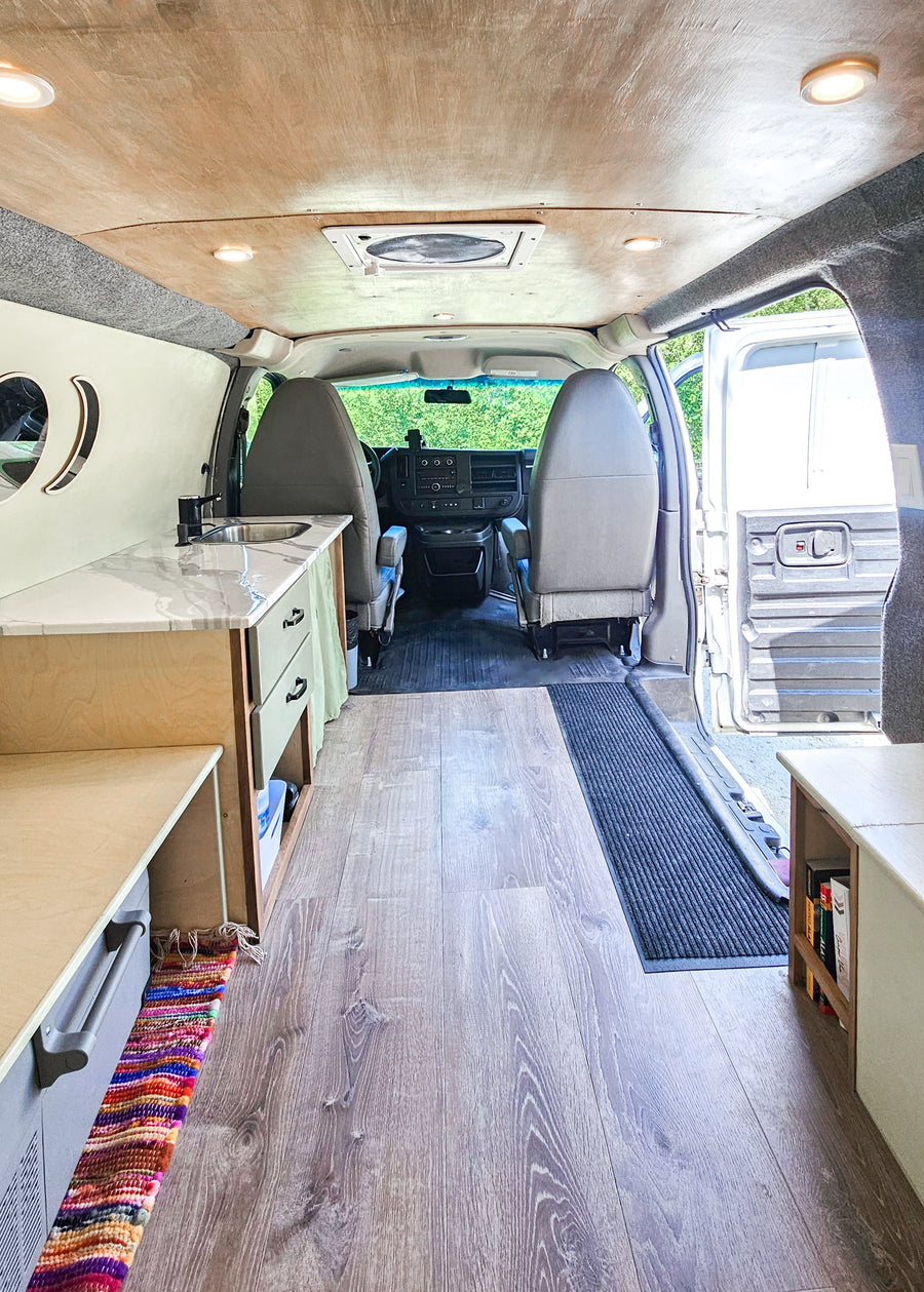Inside this RV rental van: A bright, organized camper interior with wood floors, a compact kitchen, and front seating area.