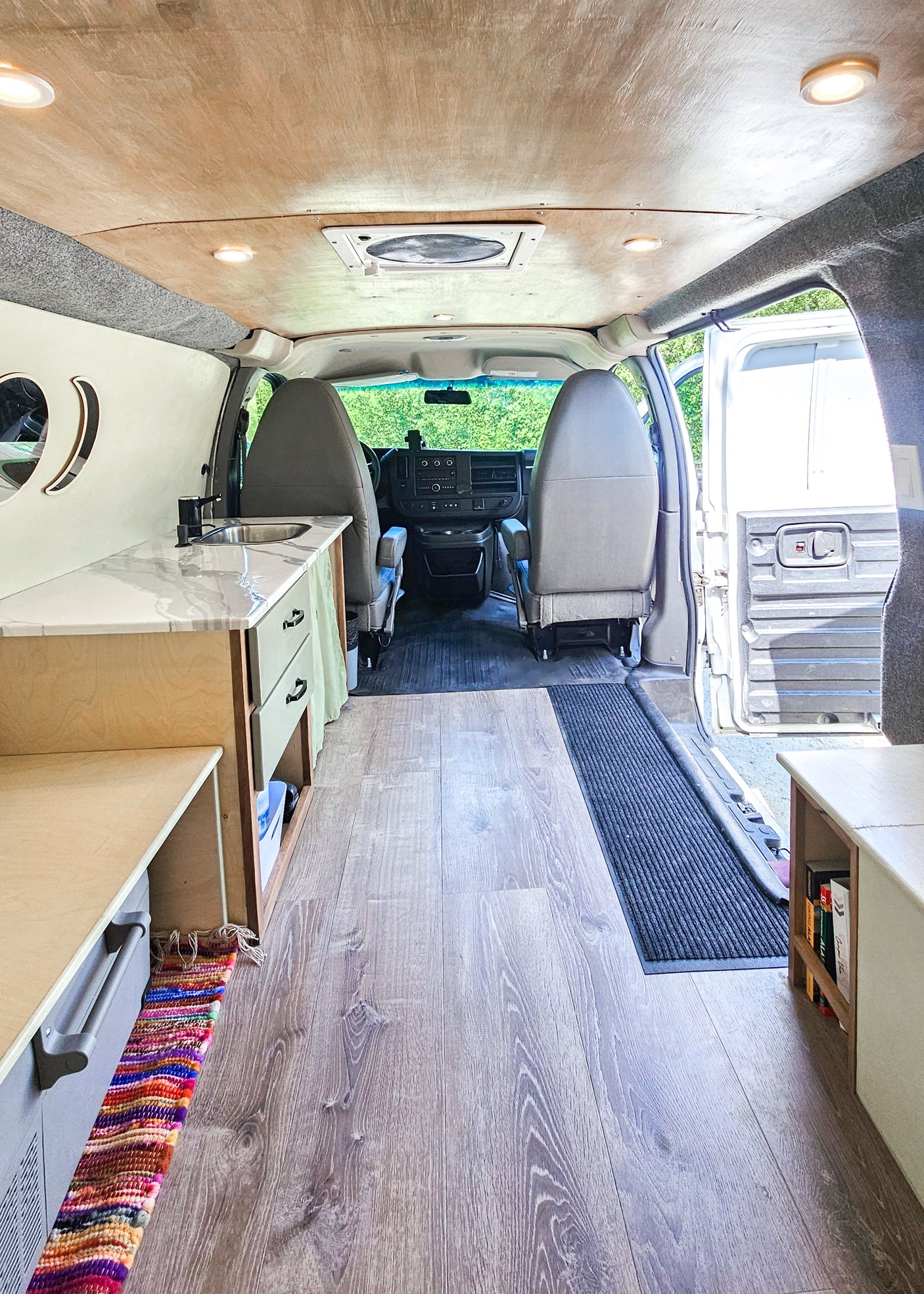 Inside this RV rental van: A bright, organized camper interior with wood floors, a compact kitchen, and front seating area.