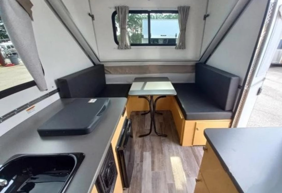 and kids playing on a mat. Great outdoor camping trip!|An A-Liner pop-up camper RV rental with an open door in a wooded area by water