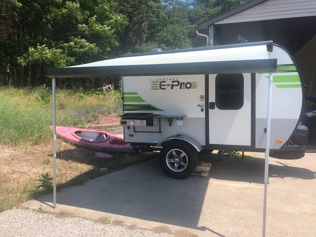 A white Flagstaff E-Pro RV rental with its awning extended over an outdoor kitchen, a pink kayak sits next to it.
