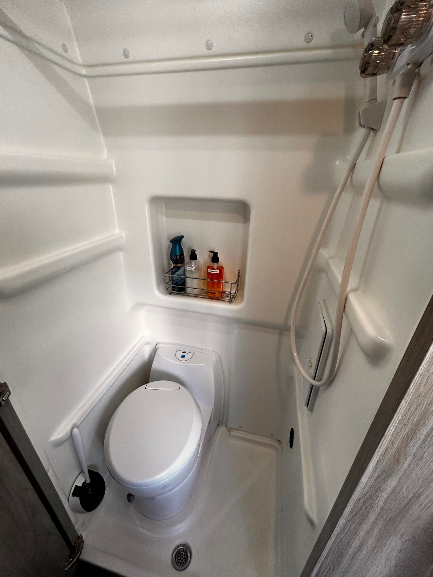 Inside an RV rental: a bright white, compact wet bath featuring a toilet, integrated shower, and toiletries shelf.