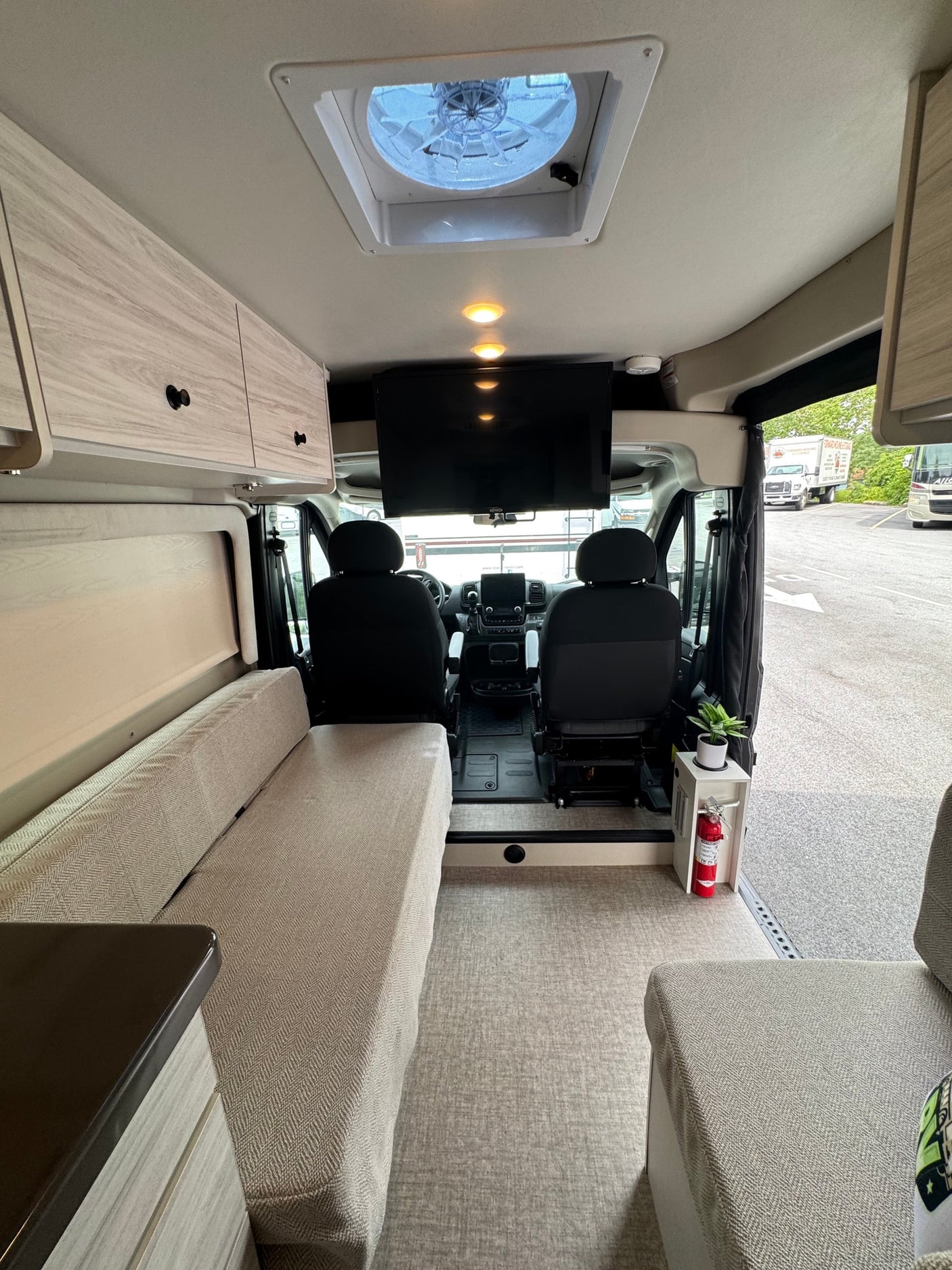 Inside a modern RV rental, showing the beige living area, cockpit, overhead TV, and ceiling fan. Ready for adventure.