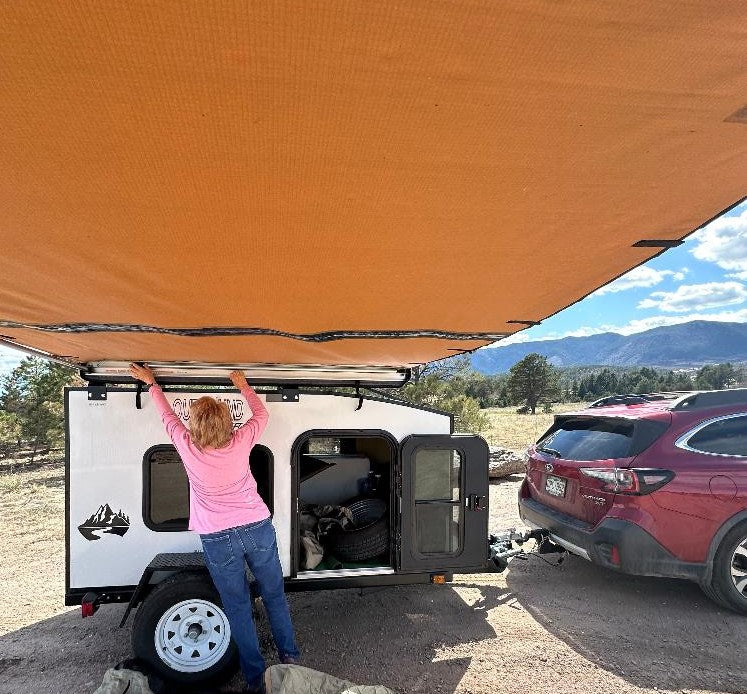 hitched to a red SUV at a scenic mountain campsite.|A red Subaru Outback tows a white Outbound Escape travel trailer — photo 6