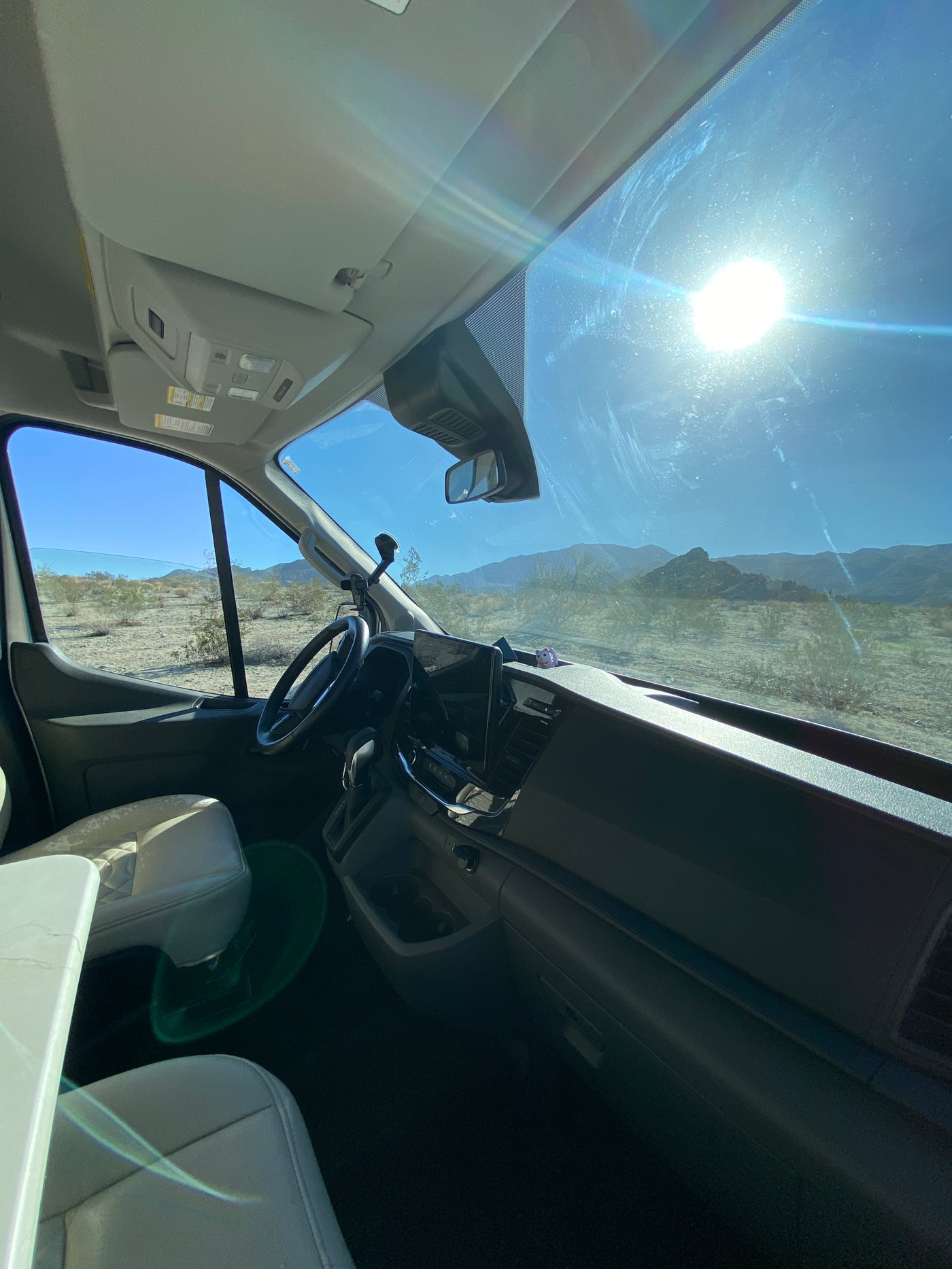 Inside a bright RV rental camper van. Sun glares on the windshield, revealing desert views and distant mountains. — photo 8