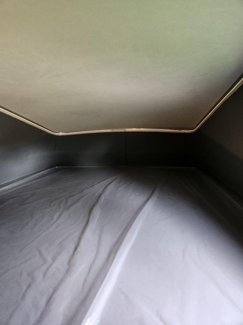 Inside an RV rental's pop-top bed: A cozy sleeping area with a light ceiling, dark sides, and a covered mattress below.