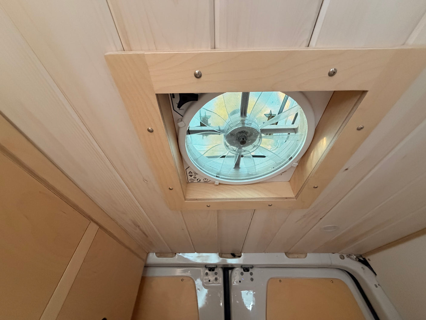 Looking up at the light wood-paneled ceiling and large, screened vent fan in this cozy RV rental interior.