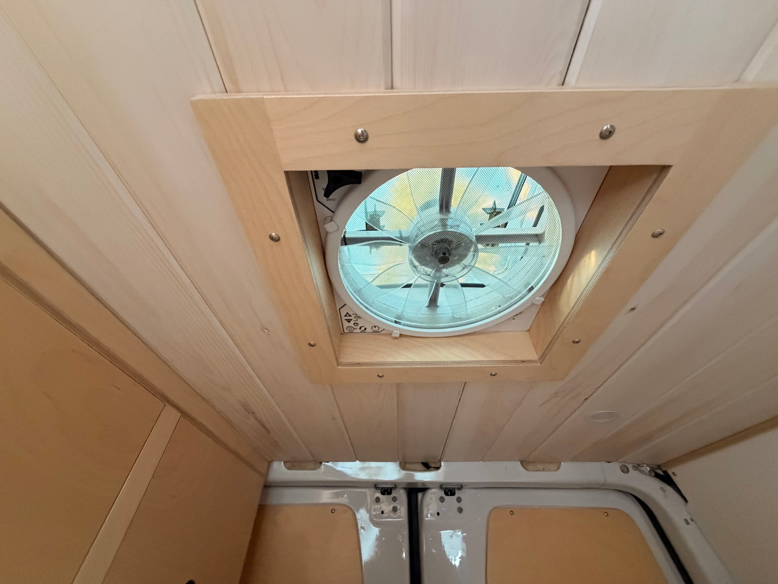 Looking up at the light wood-paneled ceiling and large, screened vent fan in this cozy RV rental interior.