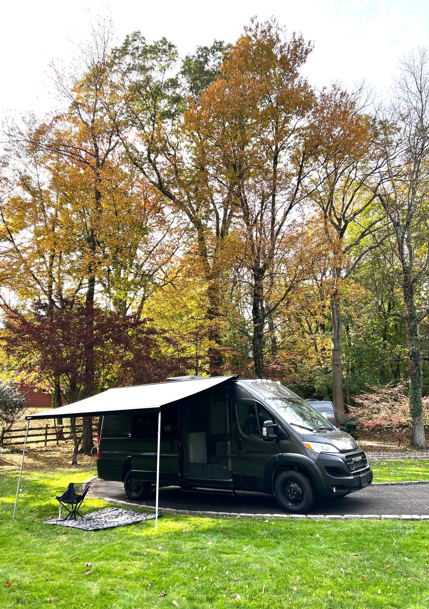 Dark gray camper van with awning extended, ready for your rv rental adventure amidst autumn trees.