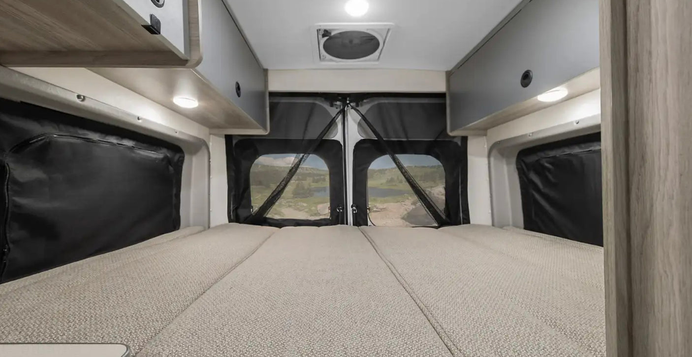 Cozy RV rental interior with a light grey bed leading to rear windows showcasing a scenic outdoor view.