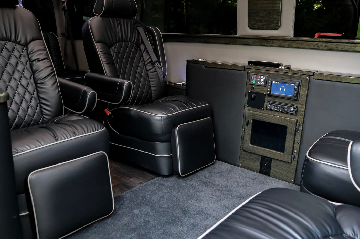 Inside a premium RV rental: spacious interior with black leather captain's chairs, diamond stitching, advanced control panel & plush carpet.