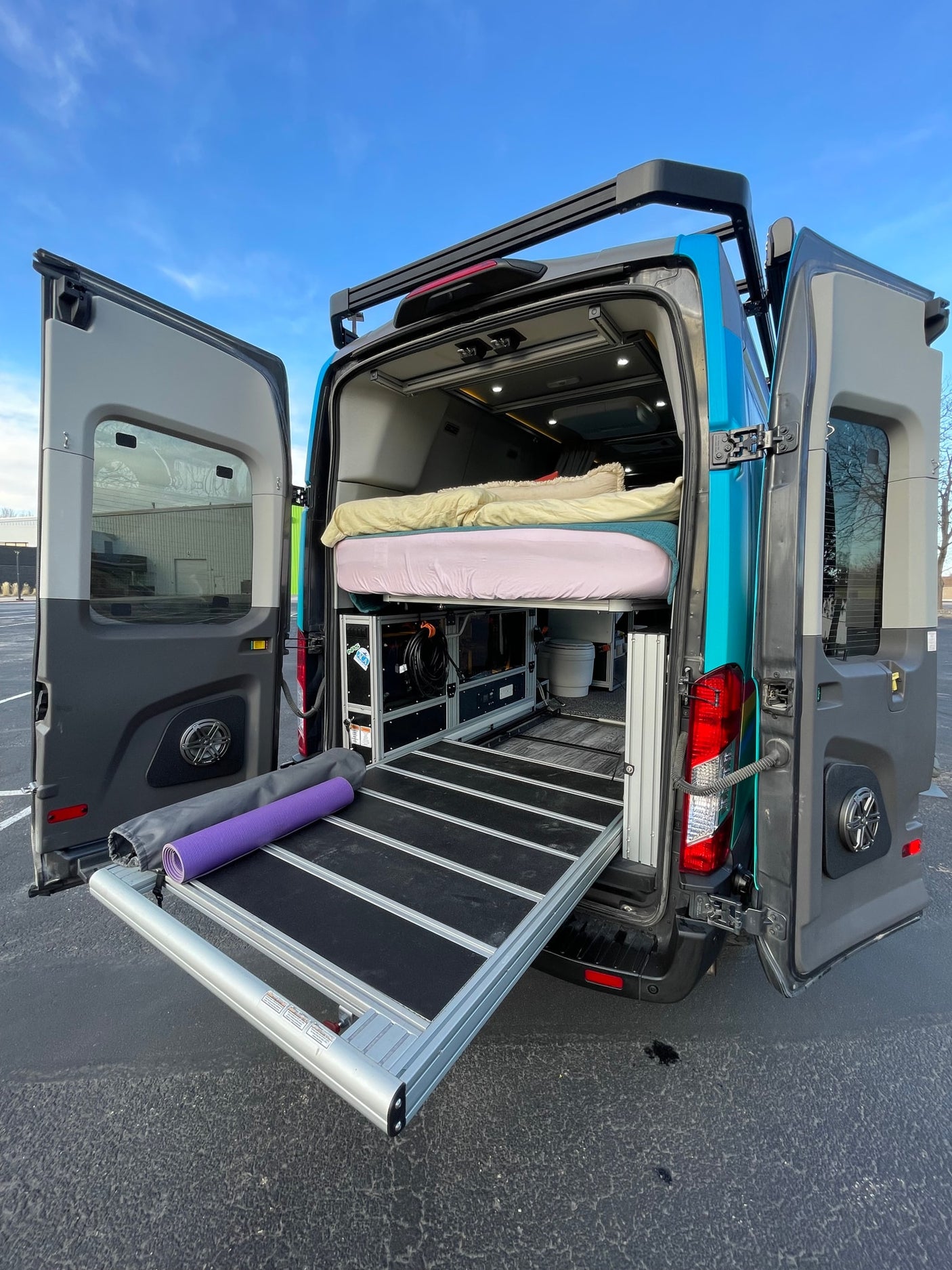This customized camper van, perfect for an RV rental, shows its clever interior storage, bed, and pull-out tray from the back.