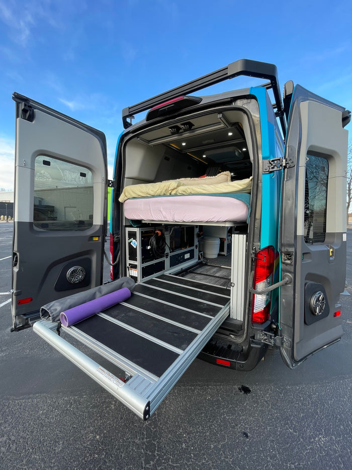 This customized camper van, perfect for an RV rental, shows its clever interior storage, bed, and pull-out tray from the back.
