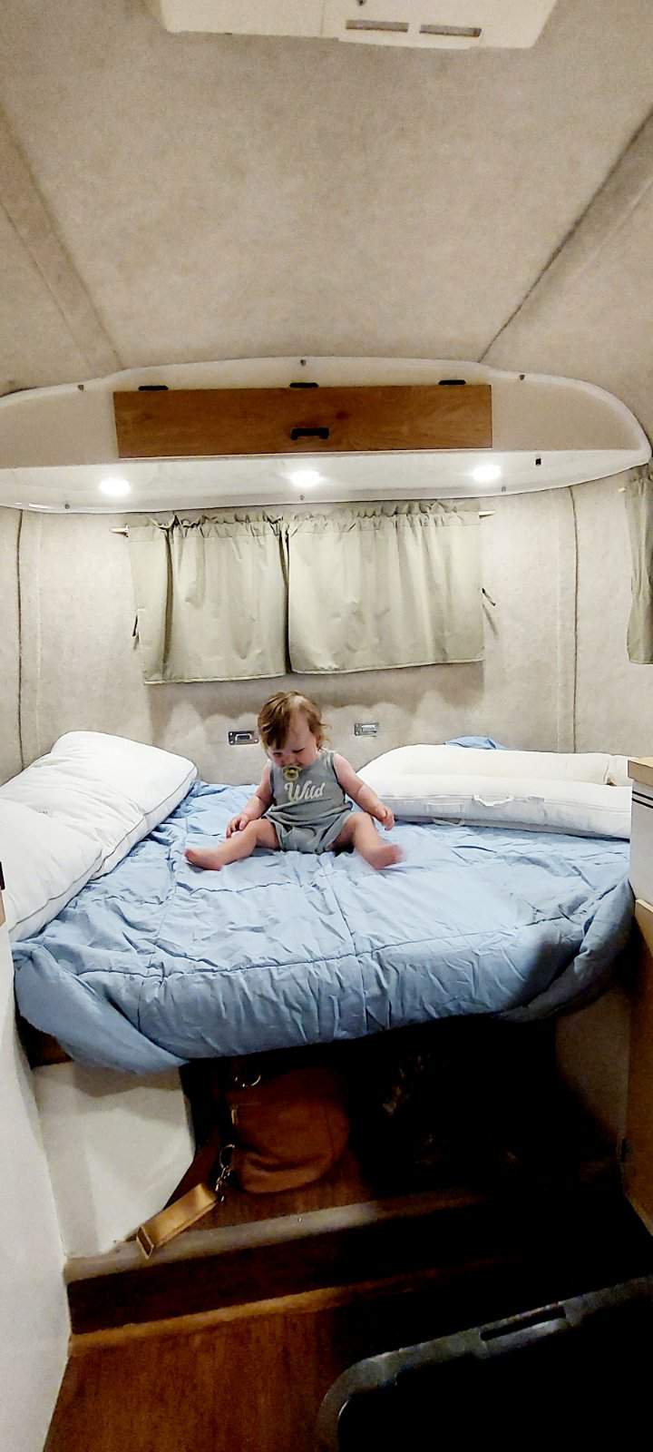 Happy baby with a pacifier on a blue bed in a cozy RV rental bedroom.