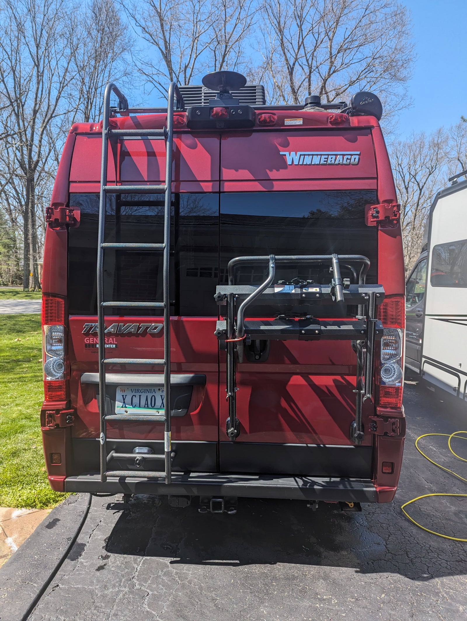 with a blue mat spread on the ground.|Rainy campground scene: a red RV rental with an awning provides shelter. A person is seated at a striped table