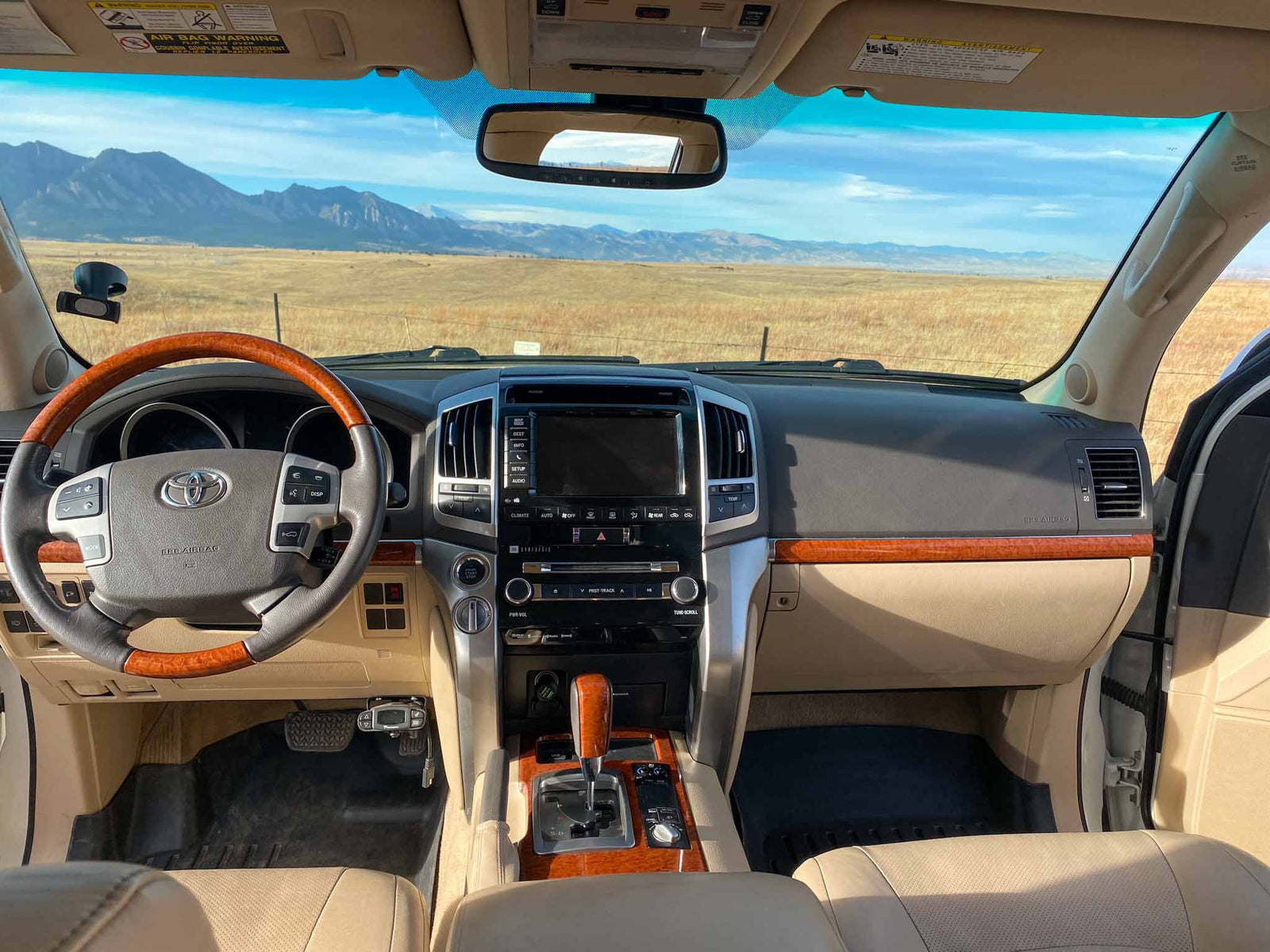 string lights illuminate a white SUV with a rooftop tent. Your RV rental adventure awaits!|Looking for an RV rental? This overlanding SUV with a deployed rooftop tent and ladder offers unique mountain adventures in fall.|RV rental tailgate cooking: A portable stove heats a pot with stunning desert mountain views. Perfect camp kitchen setup.|Luxury SUV interior on a road trip