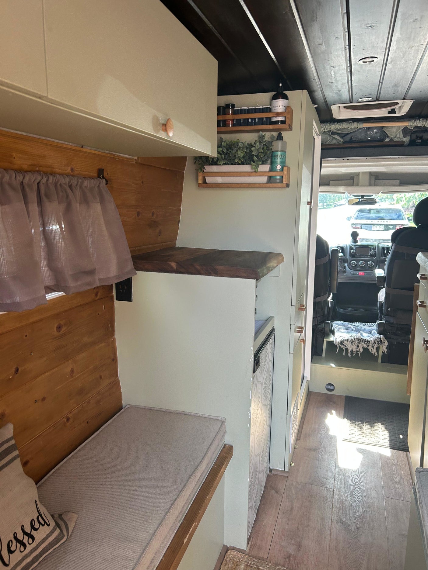Bright rv rental interior featuring sage green cabinets, wood walls, and a cozy bench, with a view to the driver's cab.