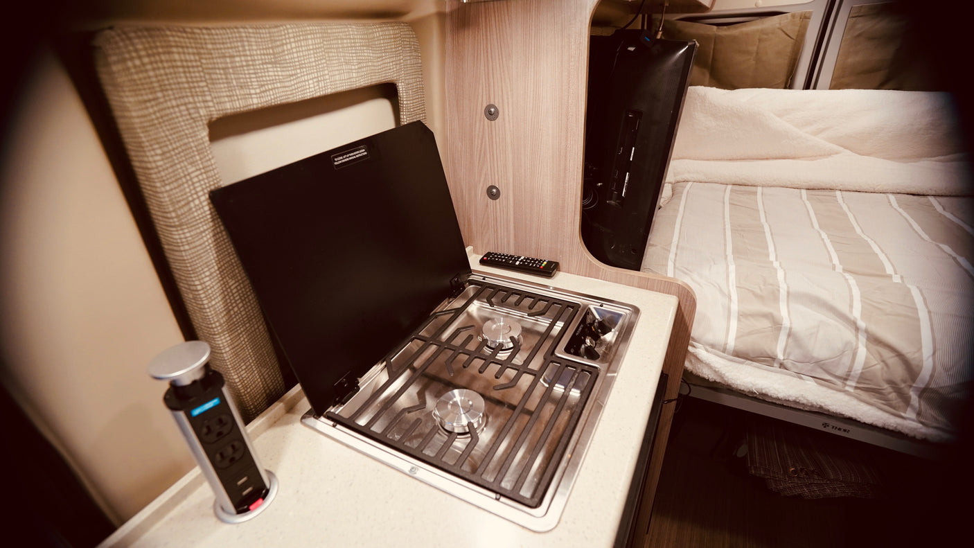 Compact kitchen with stove and pop-up outlet, plus a cozy bed with TV, make this RV rental comfortable.