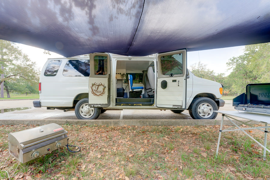 This rv rental camper van is set up for a comfortable outdoor experience with an awning, portable grill, and camp stove.