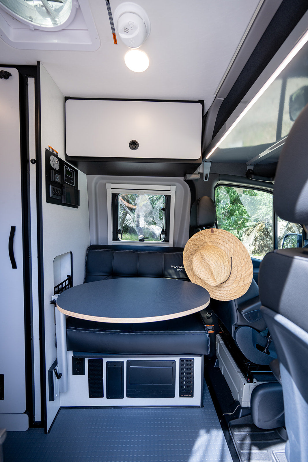 Cozy camper van RV rental interior: dinette with table & seating, overhead storage, and window view for road trips.