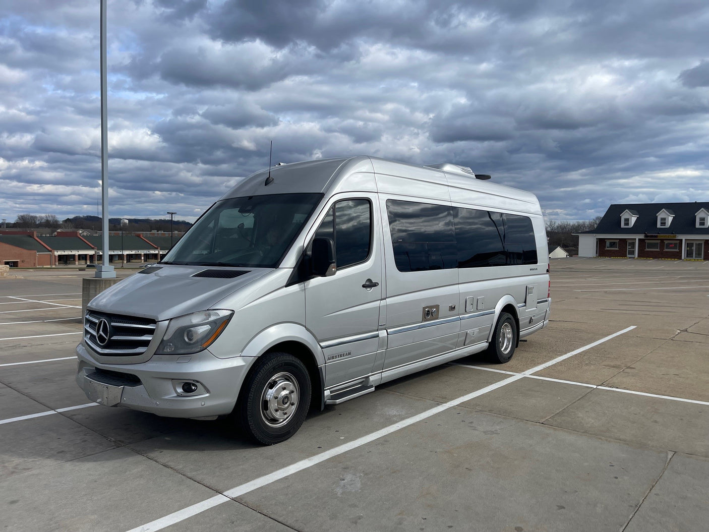 A silver Mercedes-Benz Sprinter Airstream RV rental is parked in a lot under a cloudy sky.|Silver Airstream Interstate luxury RV rental