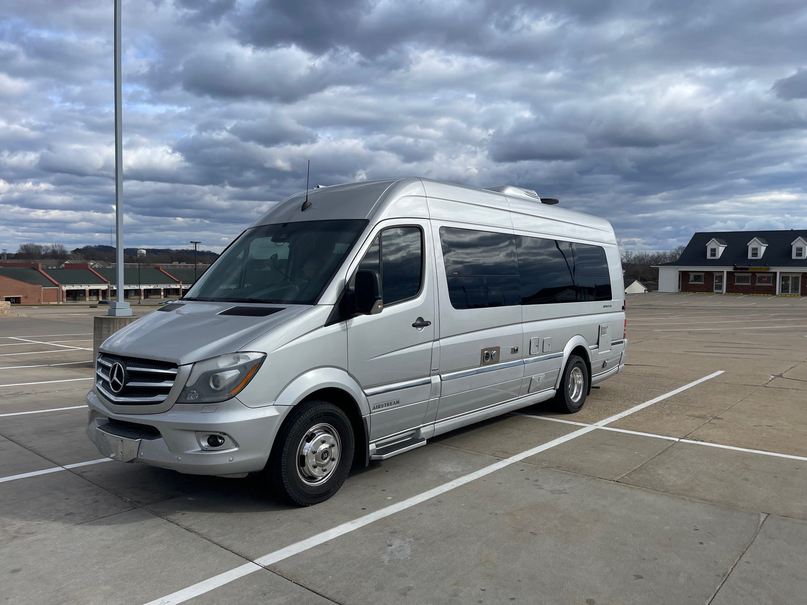 A silver Mercedes-Benz Sprinter Airstream RV rental is parked in a lot under a cloudy sky.|Silver Airstream Interstate luxury RV rental