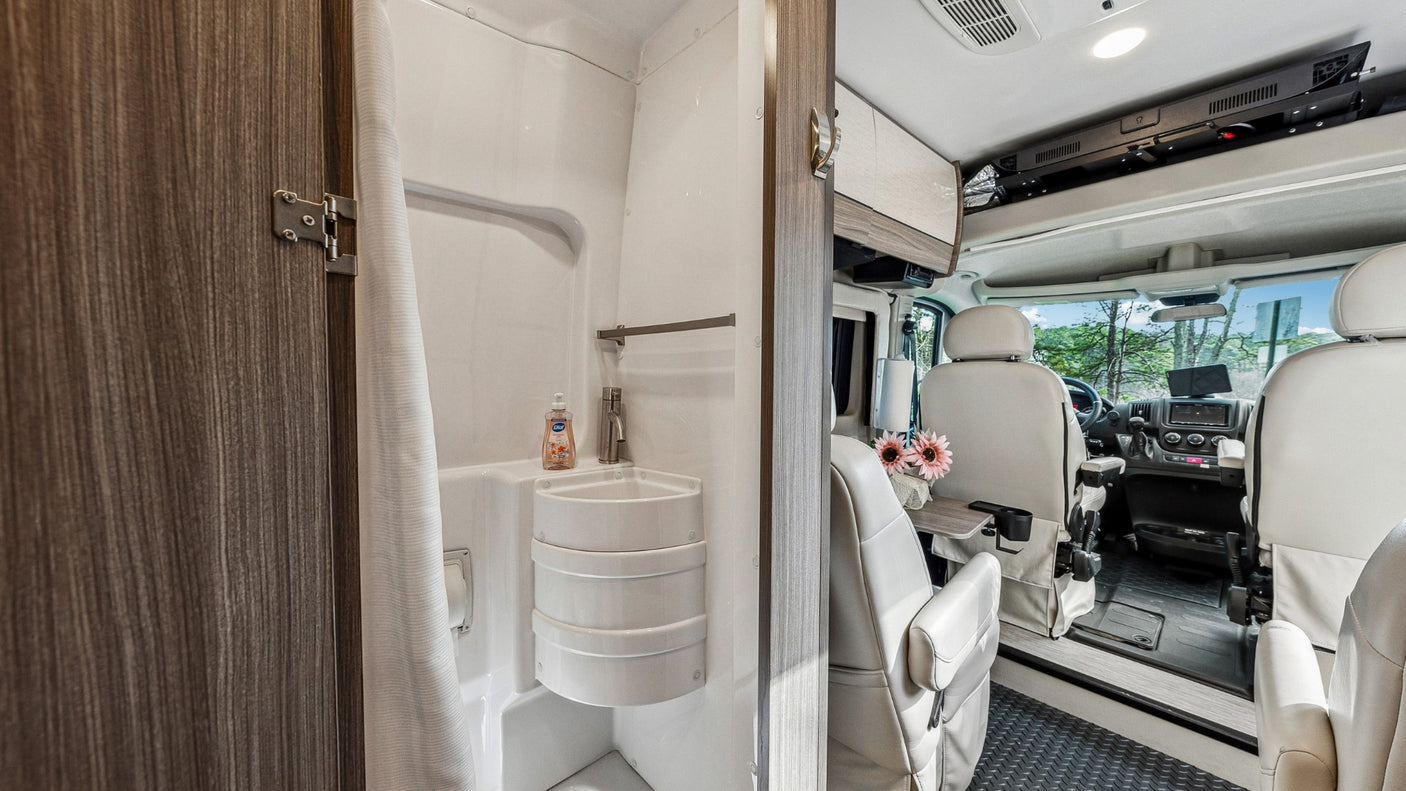 RV rental interior: compact bathroom with shower/sink, leading to front cockpit with swivel seats. Ready for your next road trip!