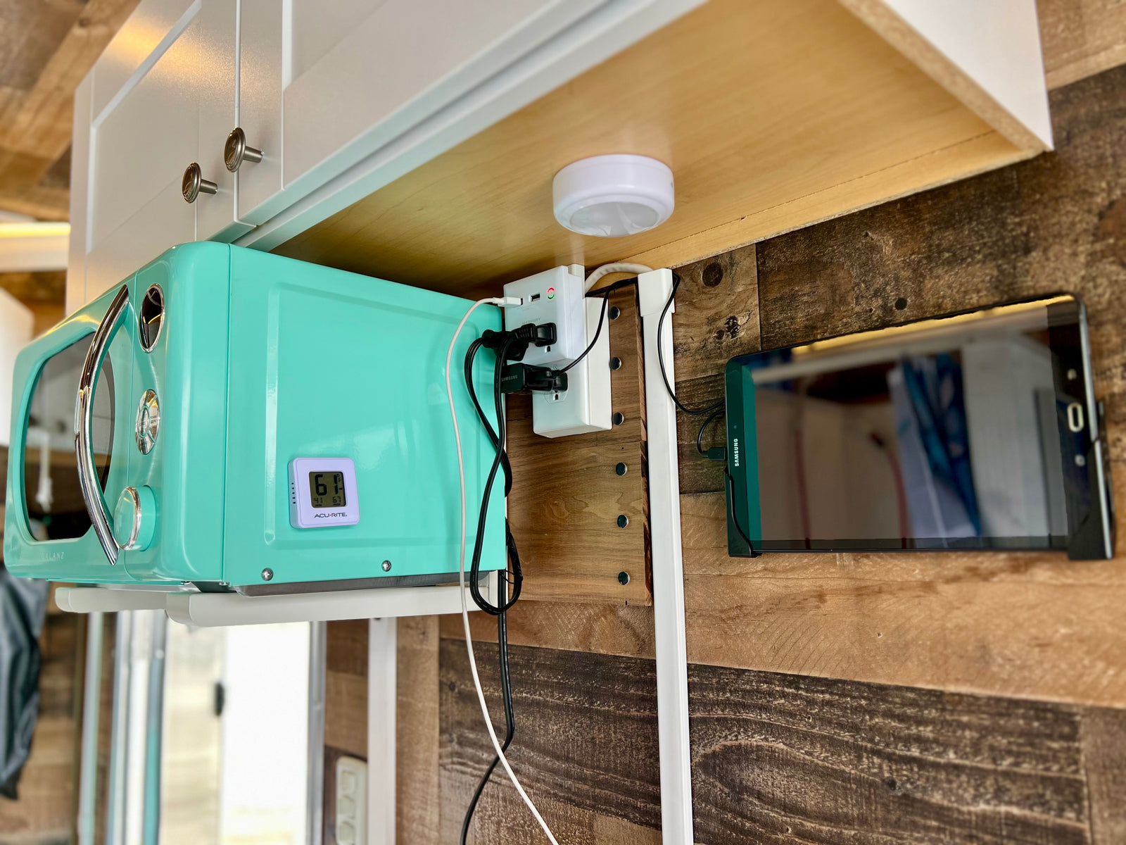 Organized tech setup in an **rv rental** kitchen: turquoise microwave, multi-outlet power hub, and Samsung tablet.