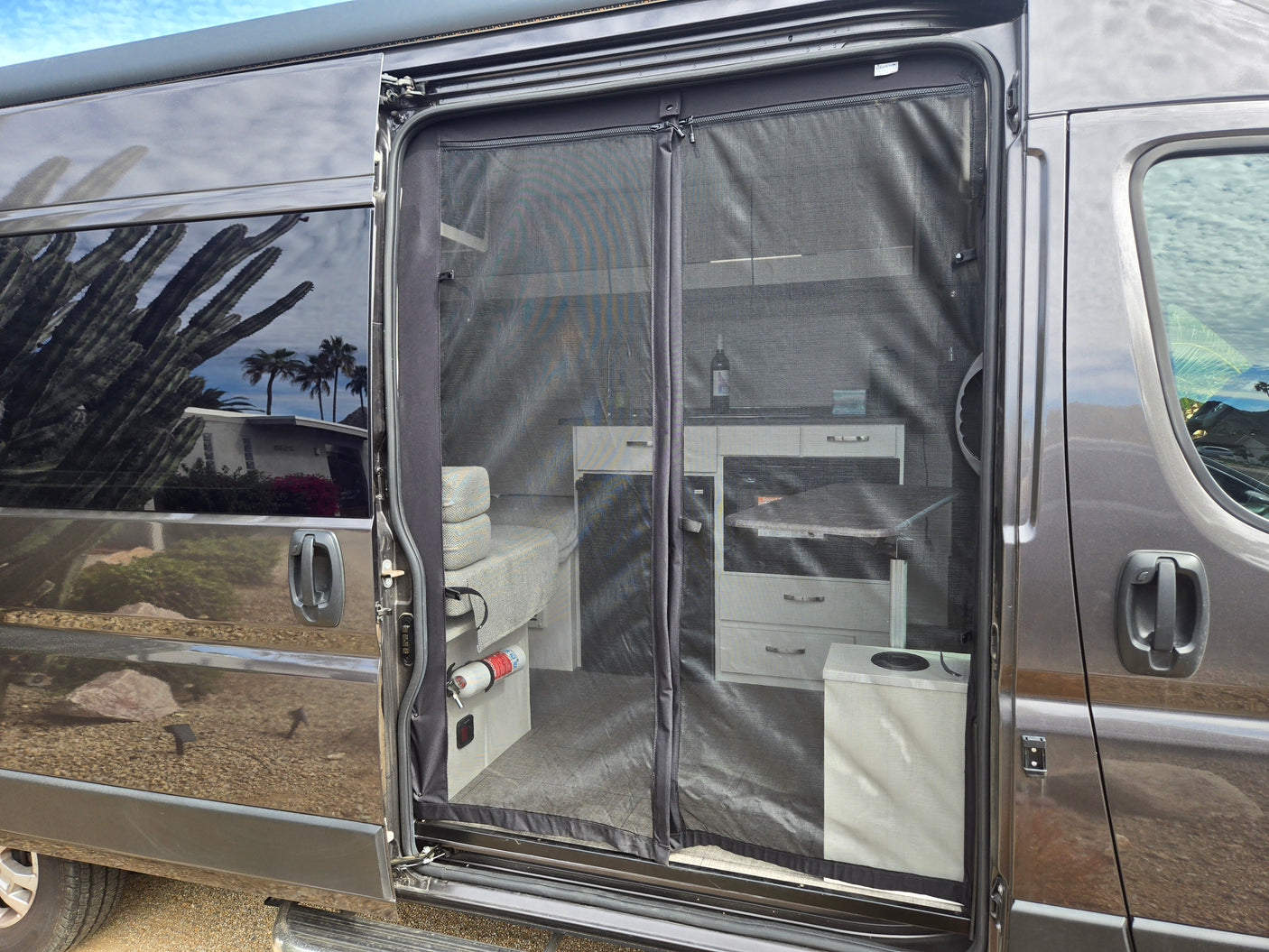 RV rental: sliding door open, magnetic screen reveals organized interior with kitchen, seating, and fire extinguisher. Ready for adventure.